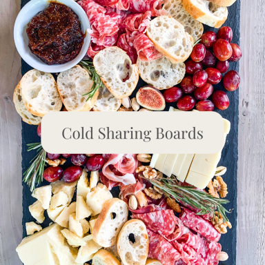 A variety of meats, cheeses, bread, grapes, and jam on a wooden board.