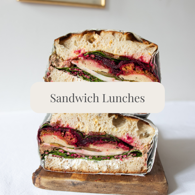 Stacked sandwich with layers of greens, meat, and colourful spread on rustic bread.