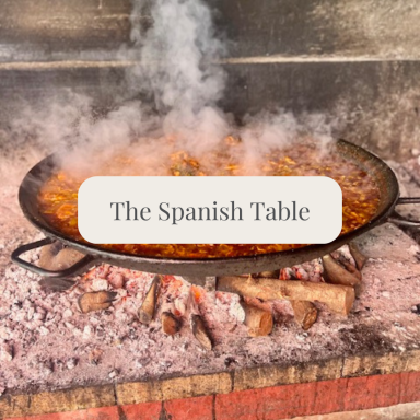 A large paella cooking over an open fire, with steam rising.